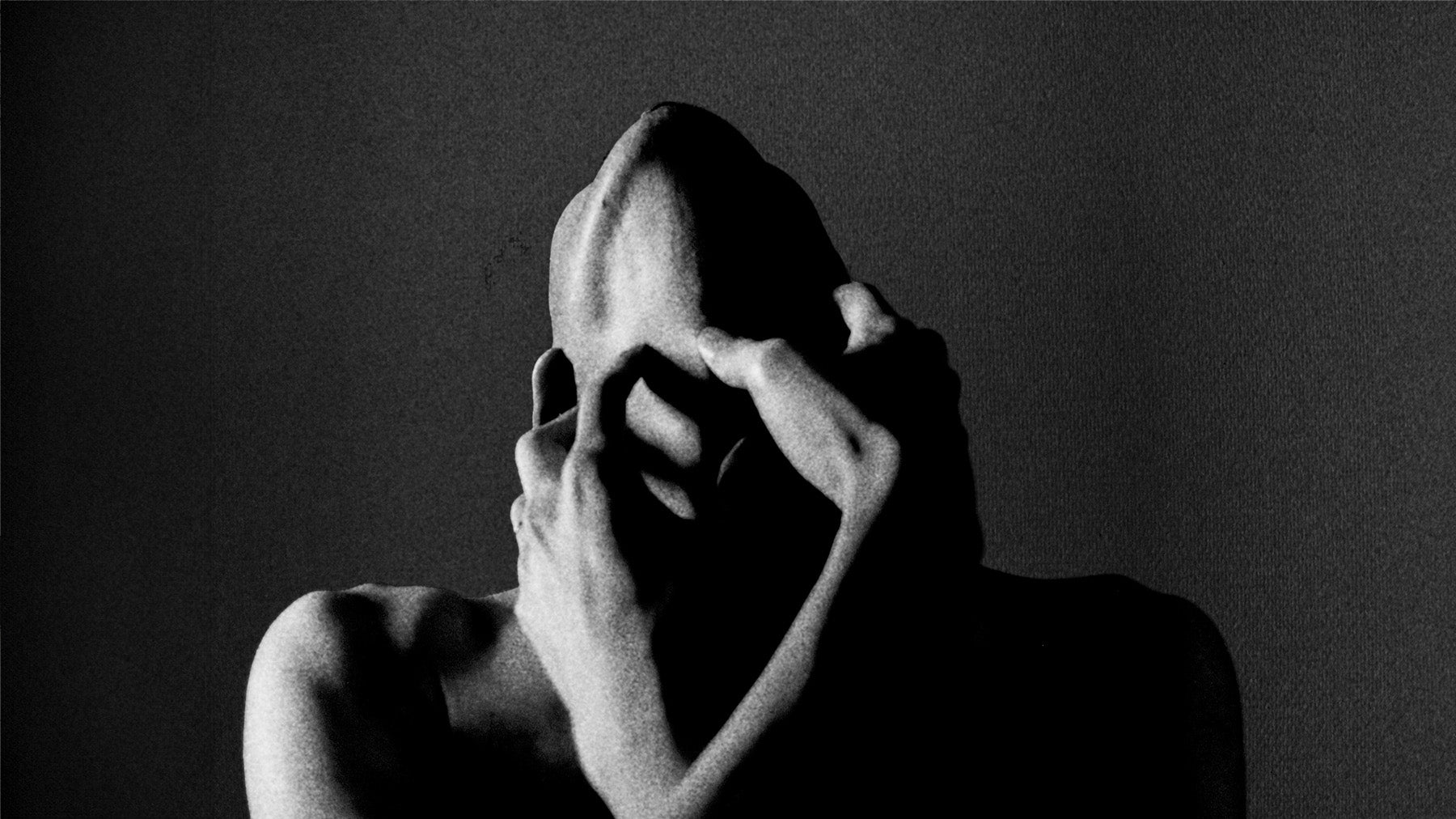 Black and white photo of a person holding their neck against a dark background